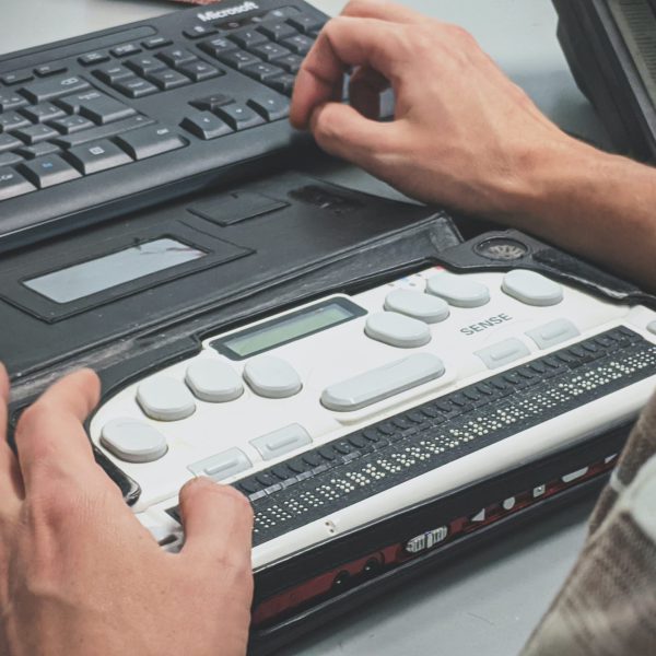 A person using a braille writer and a computer